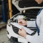Mechanic with an inspection checklist checking a used car before a St. Louis emissions test