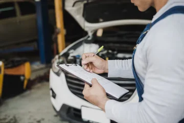 Mechanic with an inspection checklist checking a used car before a St. Louis emissions test